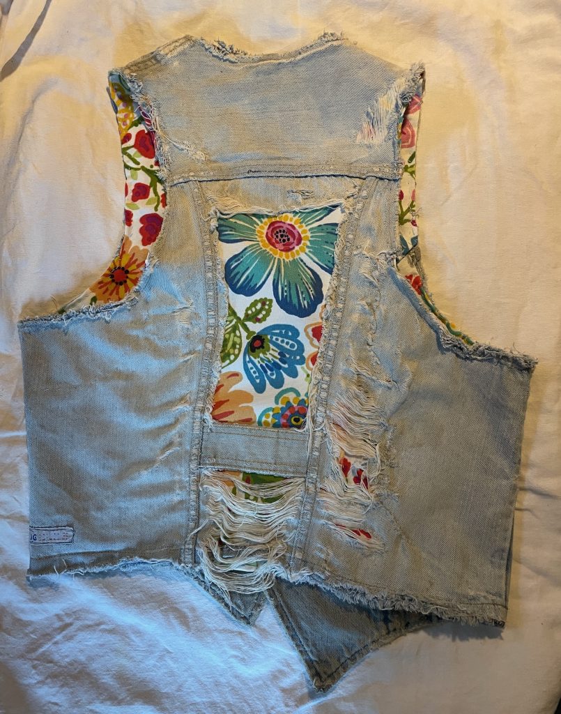 Denim vest back with exposed floral fabric and frayed texture.