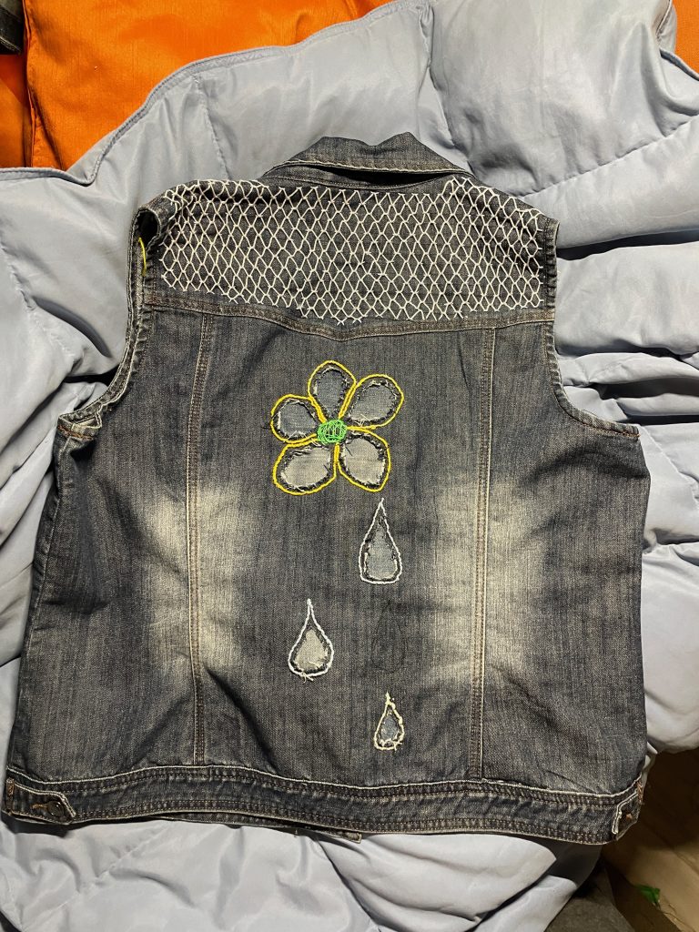 Up-cycled denim vest with embroidered flower and raindrops on back.