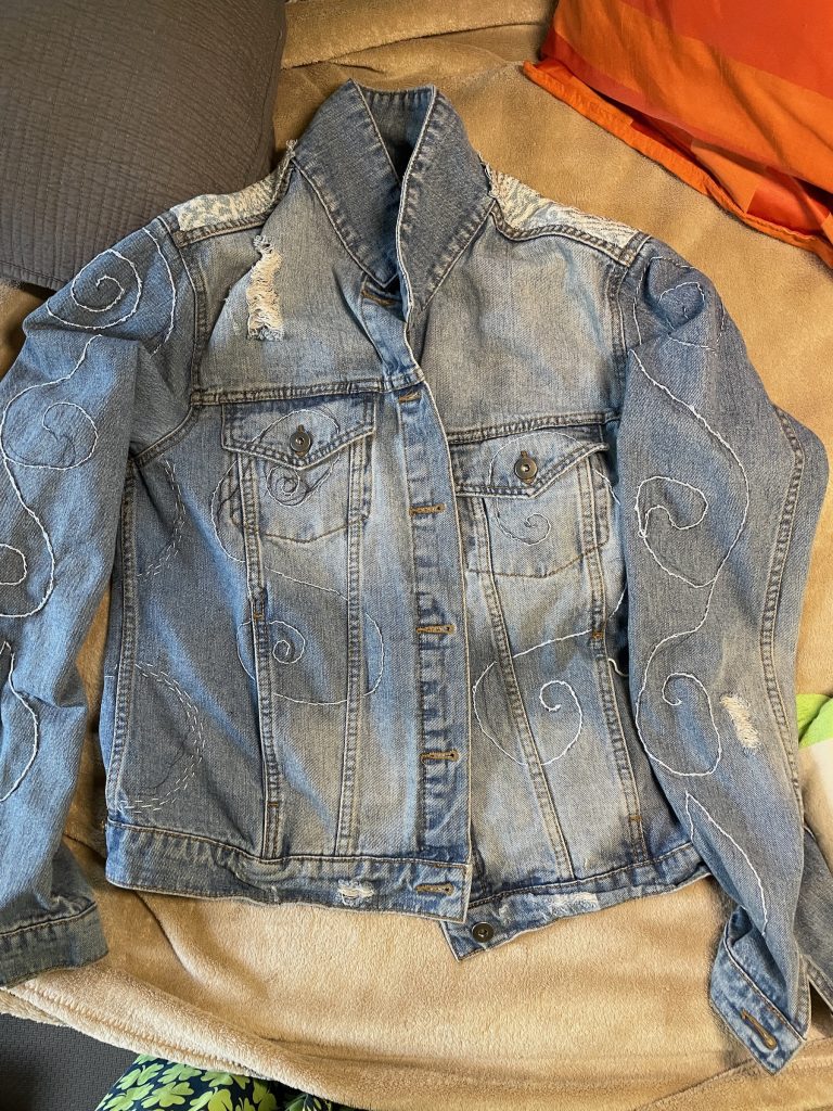 Denim jacket front with stitched swirls on sleeves and chest.